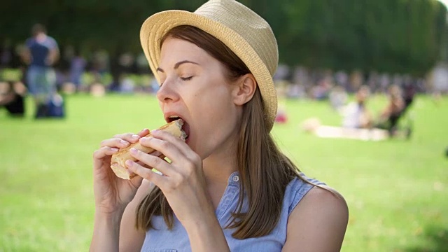 饥饿的女人在公园吃法棍面包。游客在公园享用午餐，享受夏日的阳光视频素材