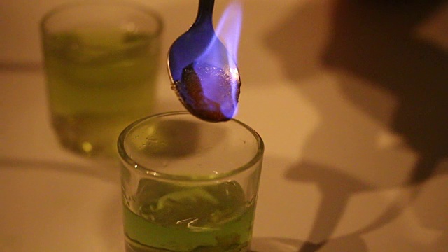 一个男人在准备苦艾酒的鸡尾酒。糖用浓饮料蘸湿，用茶匙加热即可燃烧。焦糖滴入玻璃杯。视频素材