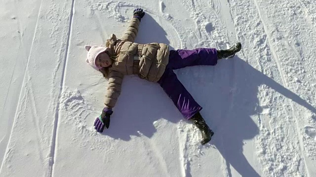 冬天快乐的女孩，孩子躺在雪地上玩，玩得开心，做雪天使视频下载