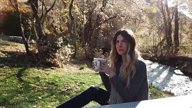 女人悠闲地坐在户外长椅上，喝着咖啡，打着电话视频下载
