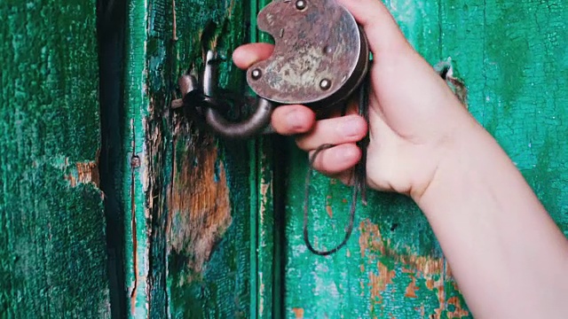 门上的老式铁锁已被绿色油漆剥落。母手开启和关闭锁视频素材