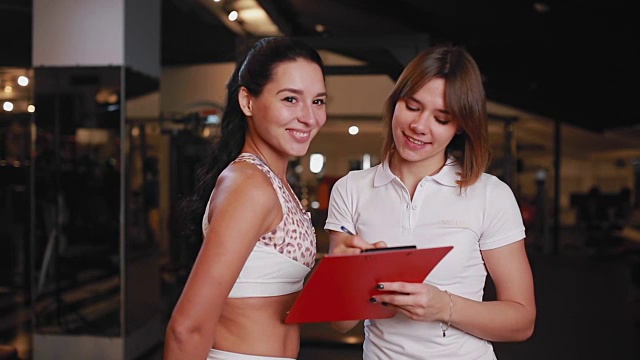 一位女性私人教练在健身房用平板电脑做笔记与一位女性客户交谈视频素材