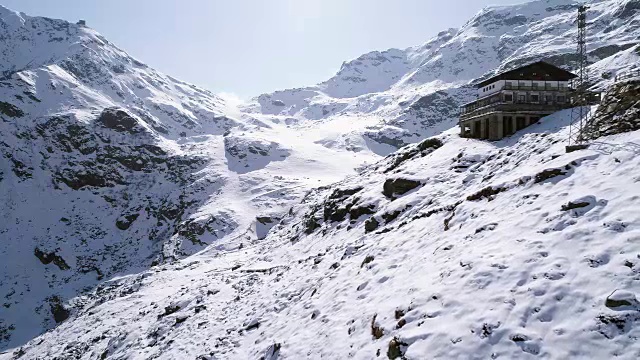 空中飞行向后移动在雪山山脊山谷附近小屋建立。冬季户外雪高山野自然景观。4k无人机飞行建立镜头视频素材