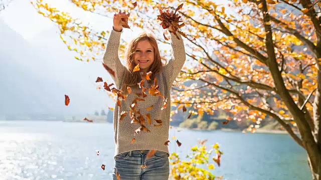微笑的女人把秋叶抛向空中视频素材