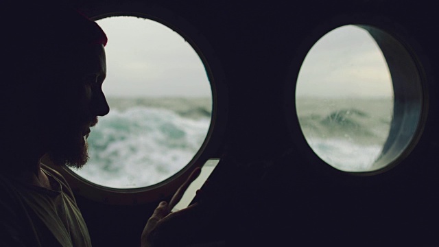 在波涛汹涌的海面上，一个人在一艘船的舷窗旁视频素材