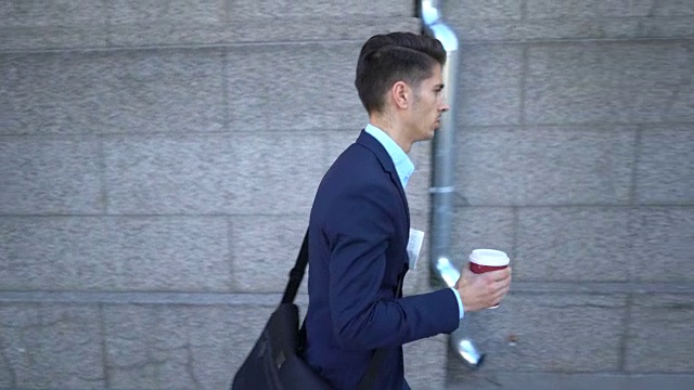 年轻的男子走在街上拿着他的咖啡和报纸视频下载