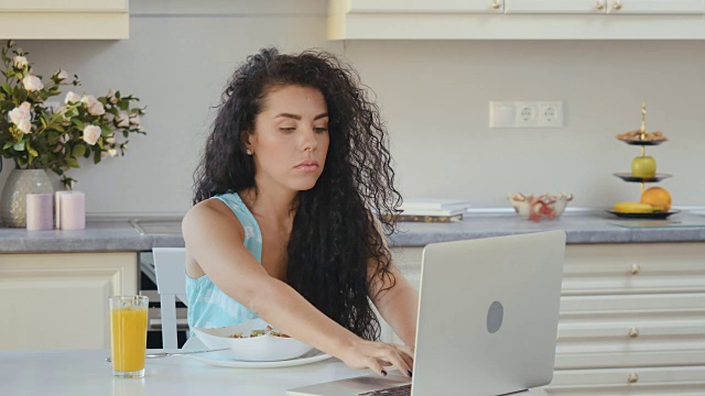 女人在早餐时喝果汁，在笔记本电脑上看电影视频素材