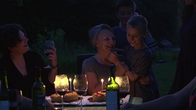 祖母生日聚会，晚上有蛋糕和蜡烛的户外大家庭视频素材