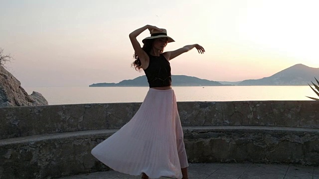 一个漂亮的女人穿着高跟鞋，穿着一件轻薄的连衣裙，戴着一顶帽子在平台上优雅地跳舞视频素材