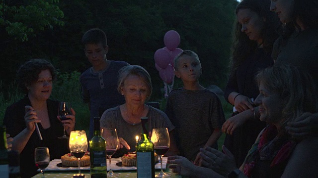祖母生日聚会，晚上有蛋糕和蜡烛的户外大家庭视频素材