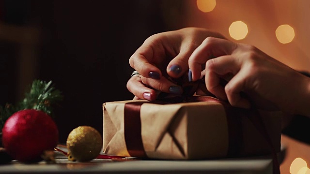 特写的背景圣诞灯妇女的手系在牛皮纸礼物上的丝带。背景是模糊的散景视频下载