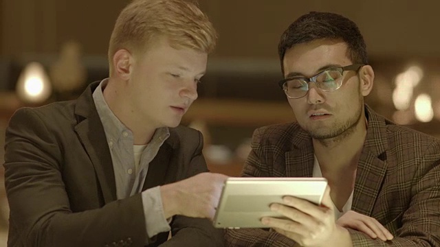 两位企业家用数字平板电脑谈生意。在公共场所会面。亚洲和高加索人。视频素材