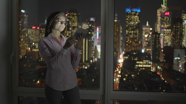 年轻的黑发女子使用数码平板电脑。在带有城市景观的公寓中使用便携式技术进行无线连接。视频素材