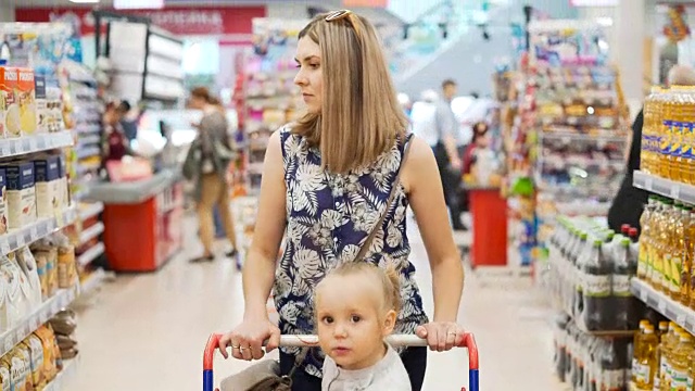 两个孩子在塑料购物车里和妈妈在市场里视频购买