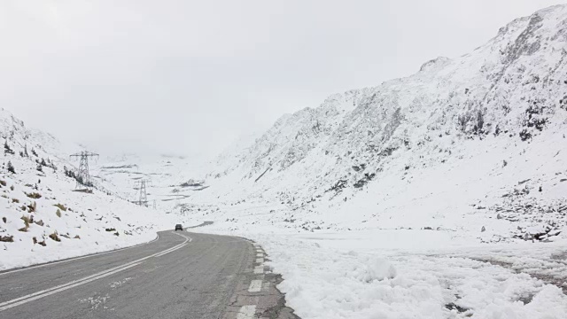 一辆黑色轿车在雪山之间的发夹弯道上行驶视频素材
