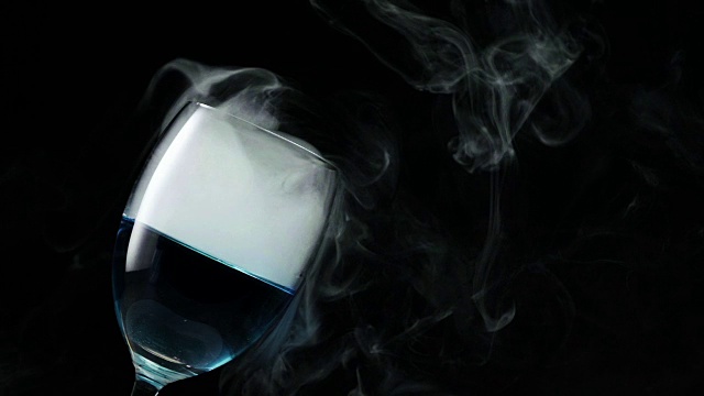 慢动作:冷蒸汽吹出香槟杯与蓝色鸡尾酒斑点深蓝色背景视频下载