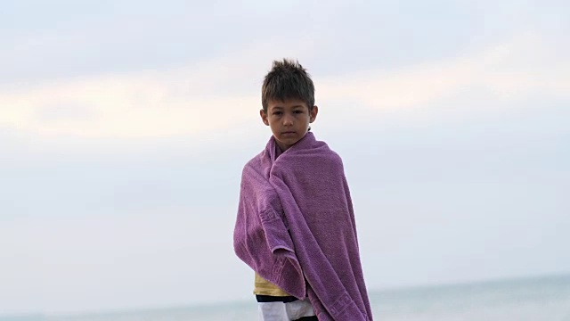疲惫悲伤的难民男孩裹着毛巾独自站在镜头前，男孩试图保持温暖视频下载