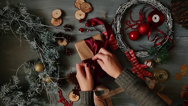 一个自上而下的计划。完全可见的桌子与装饰。女性的双手把和定型的圣诞礼物包在手纸上放在木桌上。用绷带绑好，打个蝴蝶结视频下载