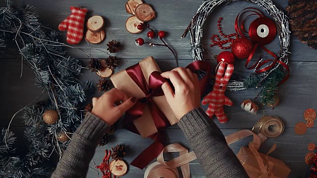 一个自上而下的计划。完全可见的桌子与装饰。女性的双手把和定型的圣诞礼物包在手纸上放在木桌上。用绷带绑好，打个蝴蝶结视频下载