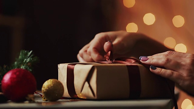 特写圣诞灯的背景，女性的手打开一个礼物从牛皮纸。背景是模糊的散景视频下载