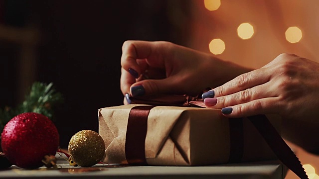 特写的背景圣诞灯妇女的手系在牛皮纸礼物上的丝带。背景是模糊的散景视频购买