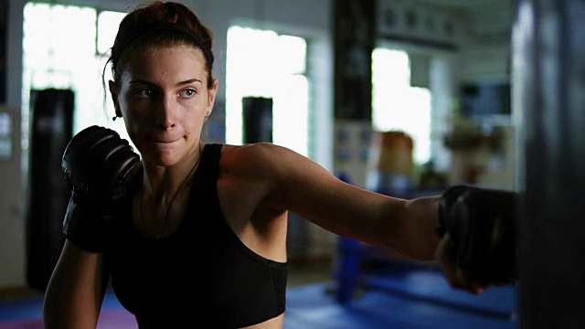 近距离观看白人女拳击手打拳击袋与她的手在手套在健身房单独。女自由搏击手的强力训练视频素材