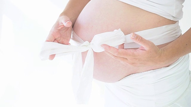一个孕妇的腹部用一个白色的蝴蝶结合拢视频下载