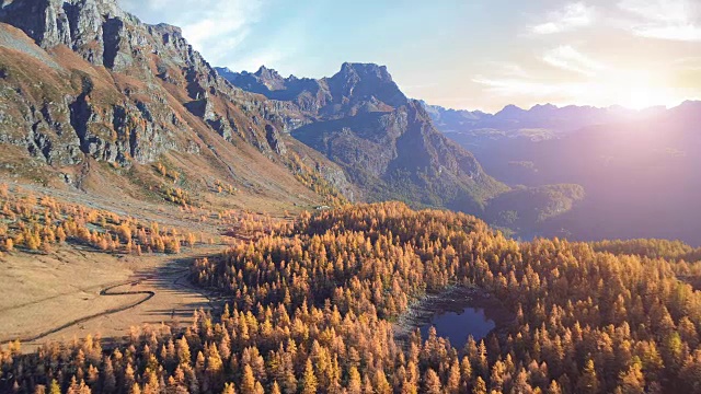 在阳光明媚的秋天，向前空中飞越高山山谷湖泊和橙色落叶松森林。阿尔卑斯山户外山野落自然在日落或日出建立。4k无人机飞行建立镜头视频素材