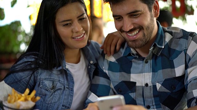 一对幸福的情侣在餐馆里用智能手机给朋友发短信玩得开心视频素材