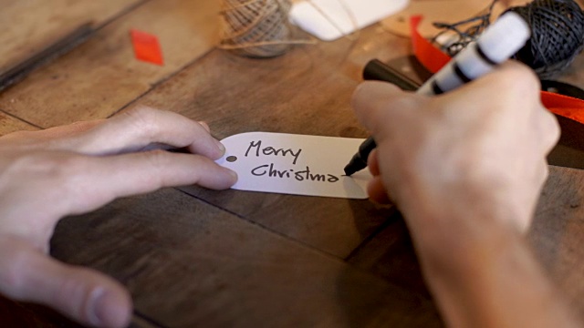年轻的成年人在舒适的室内旧木桌上的白色标签上写圣诞卡片视频下载