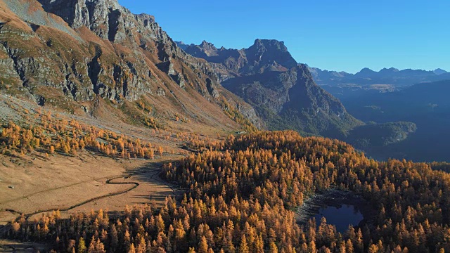 在阳光明媚的秋天，向前空中飞越高山山谷湖泊和橙色落叶松森林。阿尔卑斯山户外丰富多彩的自然景观，山野秋实的建立。4k无人机飞行建立镜头视频素材