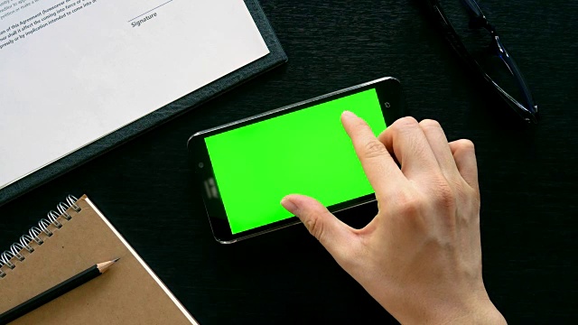 男人用手用手机用绿色屏幕在办公室桌面上查看视频素材