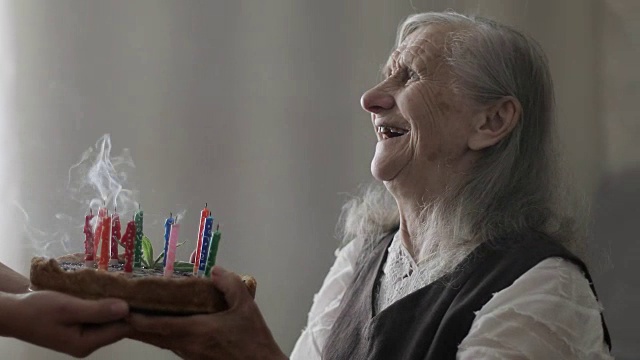 一位满头白发的快乐老妇人在吹蛋糕上的蜡烛。视频素材