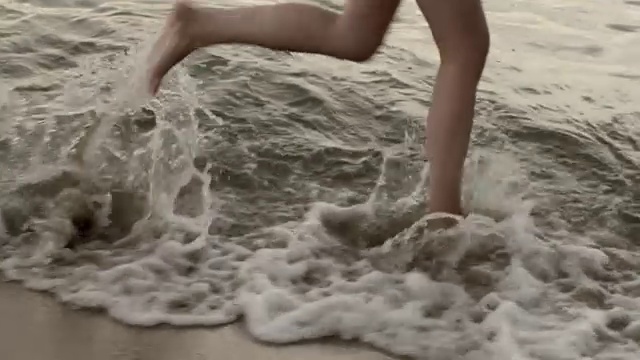 年轻女子的双腿在黎明时穿过大海视频素材