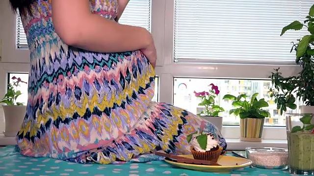 饥饿的孕妇咬着香甜的蛋糕，用柔嫩的手掌捧着她的大肚子视频素材