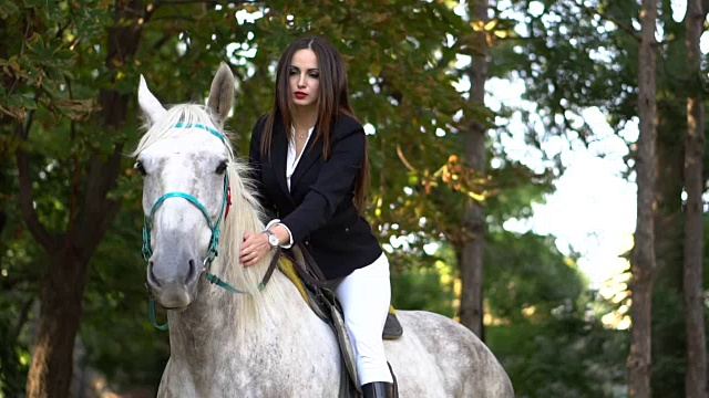 年轻的褐发调皮女孩骑和爱抚的马在公园视频下载