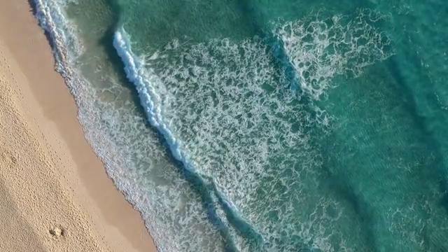 无人机拍摄的西班牙富埃特文图拉岛科拉雷霍附近的海滩。翻滚的波浪轻轻拍打着沙滩。海底可见沙质纹理。视频素材