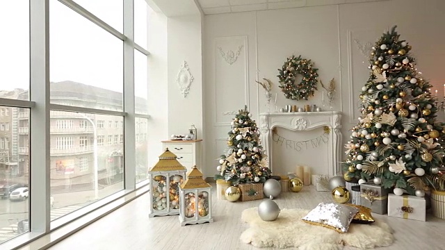 时尚的白色圣诞室内装饰冷杉树，壁炉，灯笼，灯，蜡烛，花环，肿块和礼物。圣诞树上挂满了金色的装饰品、彩灯和花环。新年前夕视频下载