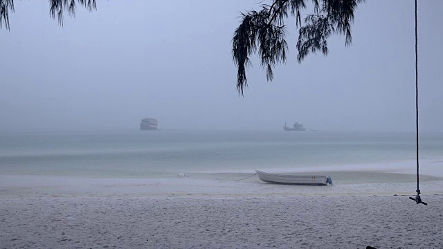 大雨下的沙滩上的小船和前景中摇摆的树视频素材