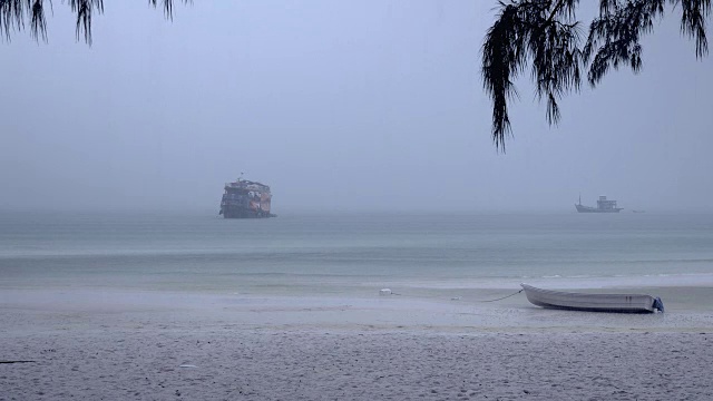 一艘小船在强降雨下停靠在沙滩上，背景是一艘正在靠岸的游轮视频素材