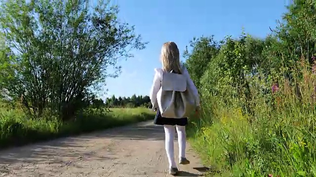 一个金发碧眼的小女孩在穿过田野的沙路上上学。视频素材