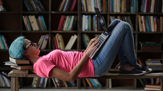 可爱的女孩躺在图书馆的长椅上，拿着笔记本电脑视频素材