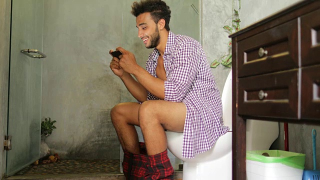 坐在马桶上的男人用手机用智能手机年轻的拉丁男人在玩游戏视频下载
