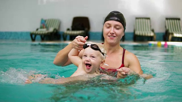 慢动作拍摄的快乐微笑的孩子和他的母亲在游泳池游泳。年轻的母亲正在水中帮他转个身，然后把他抬起来视频素材