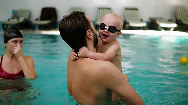 一位年轻的母亲正在向她的小儿子展示如何潜入游泳池的水里，而他就坐在边境上。他跳进水里，游泳，然后他的父亲把他从水里抬起来视频素材
