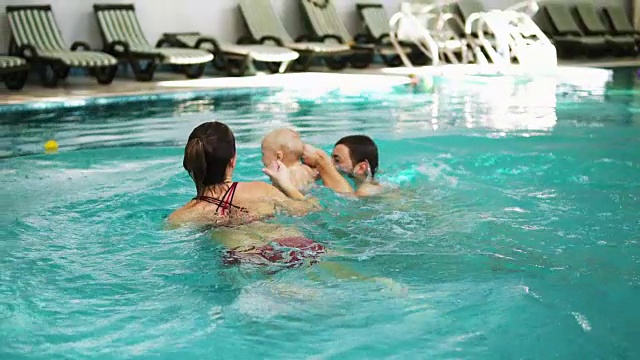 健康的年轻家庭和他们的孩子手牵着手潜入游泳池的水里。父母正在教他们的孩子如何游泳视频素材