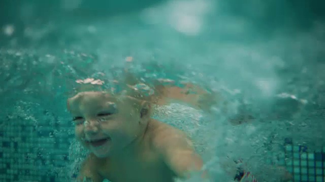可爱的金发小孩正在游泳池里跳水，直到他妈妈把他从水里抬起来。一个水下拍摄视频素材