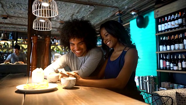 一对情侣在一家餐馆里微笑着看智能手机上的照片视频素材