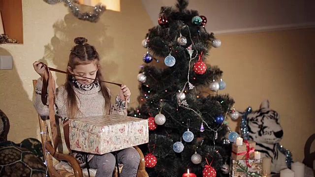 圣诞树旁的美丽小女孩打开了一个礼物盒，里面装着圣诞老人送的新年礼物视频素材