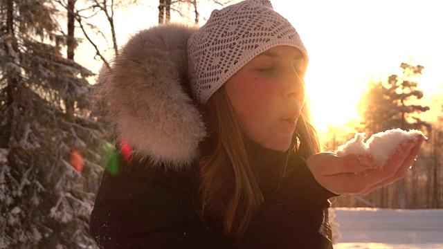 慢镜头:在神奇的冬天，年轻女子在夕阳下吹着雪花视频素材
